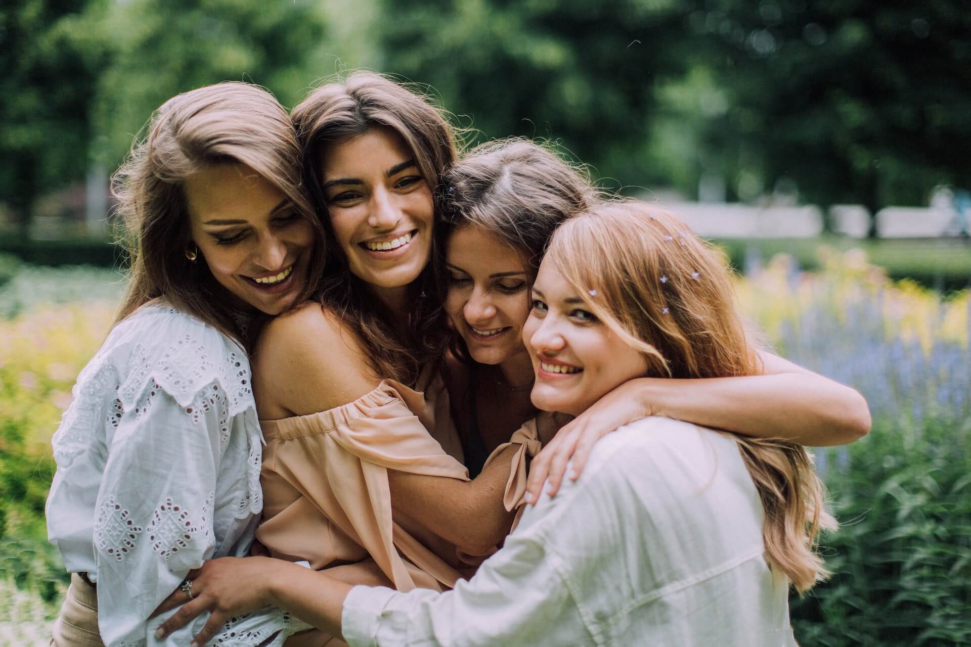 A group of 4 women hugging each other near a field