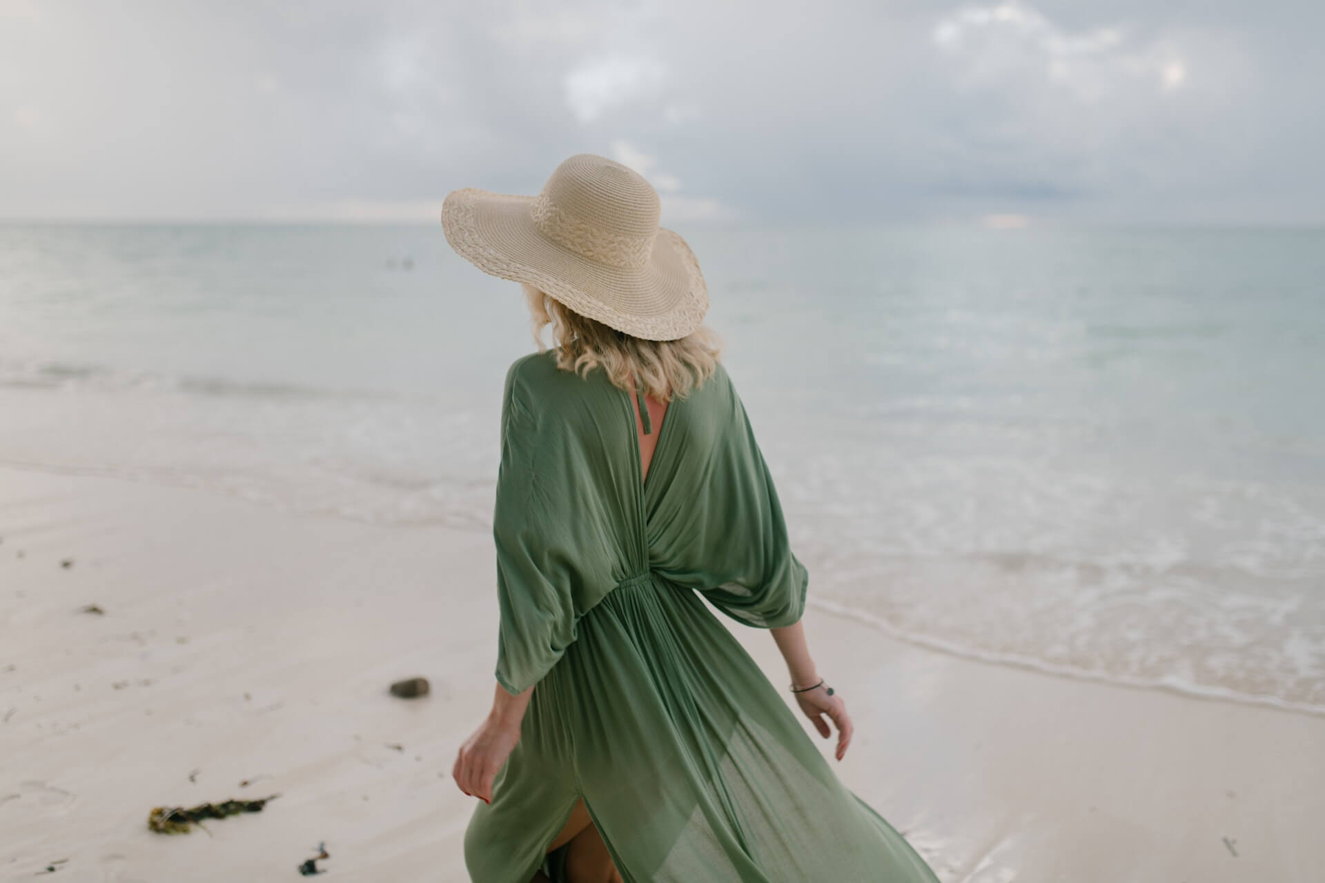 Woman with beige hat and green dress at the beach