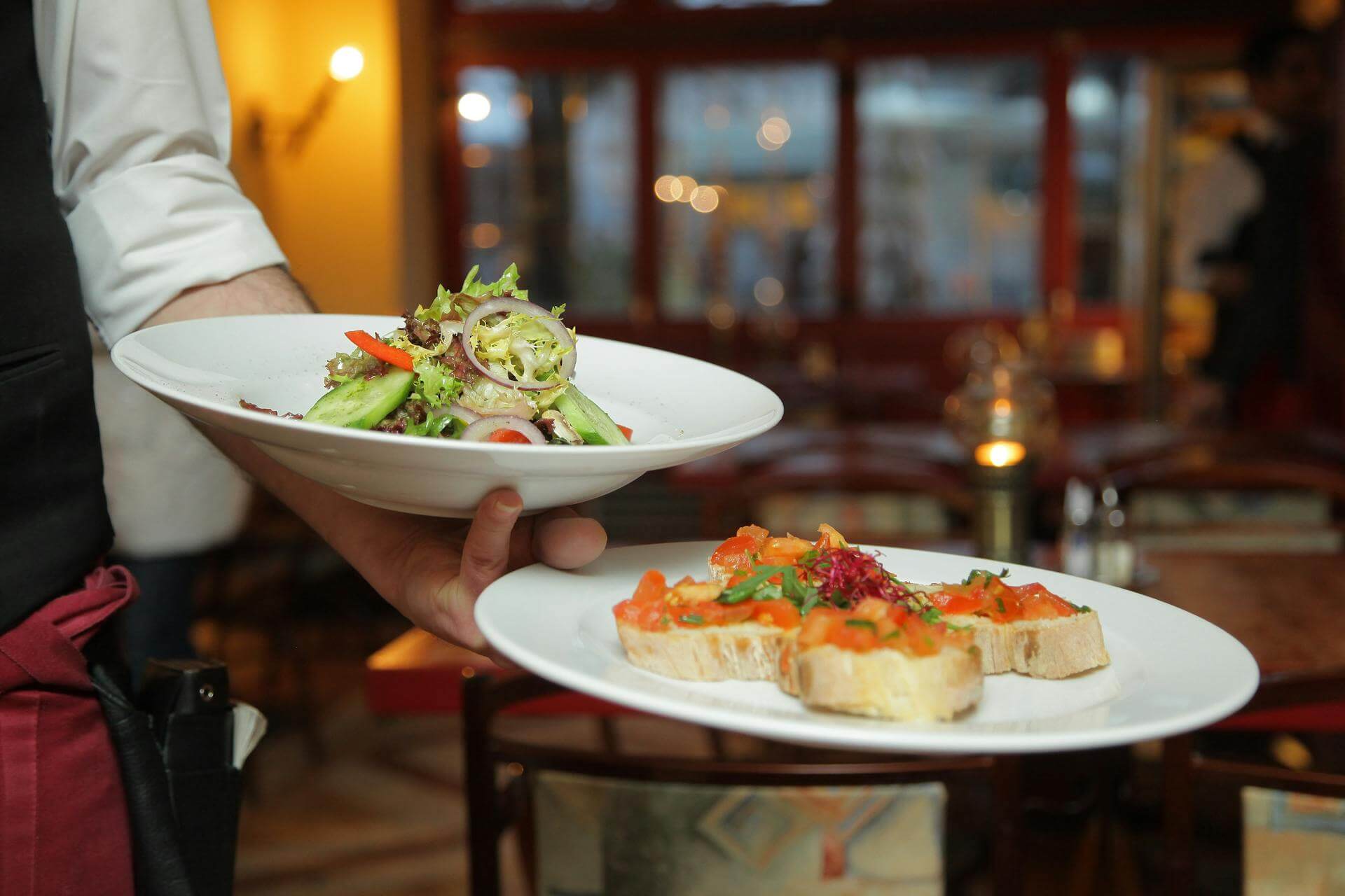 A waiter holding two plates of food in a restaurant