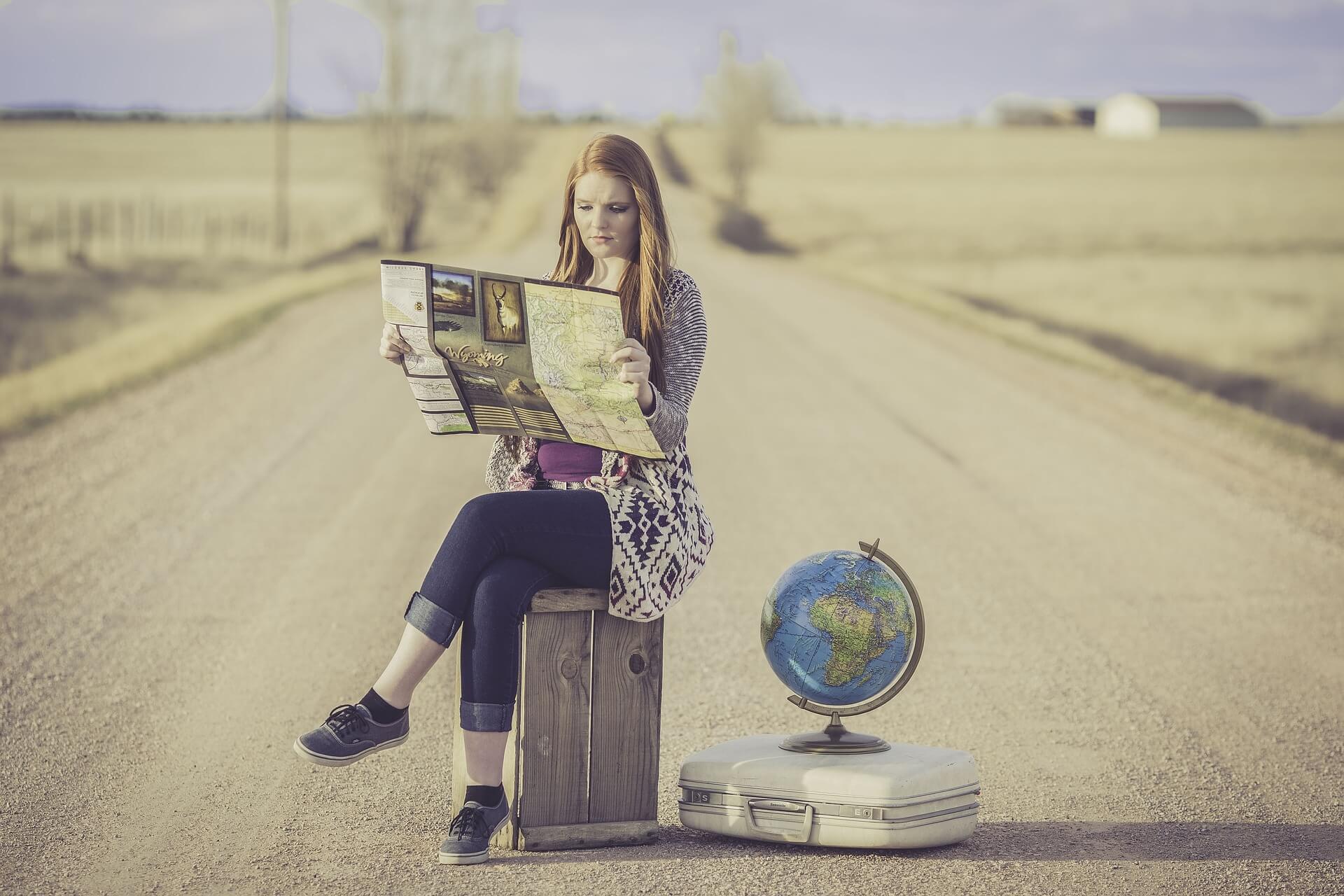 A woman on the road with a map, a globe, and a suitcase.