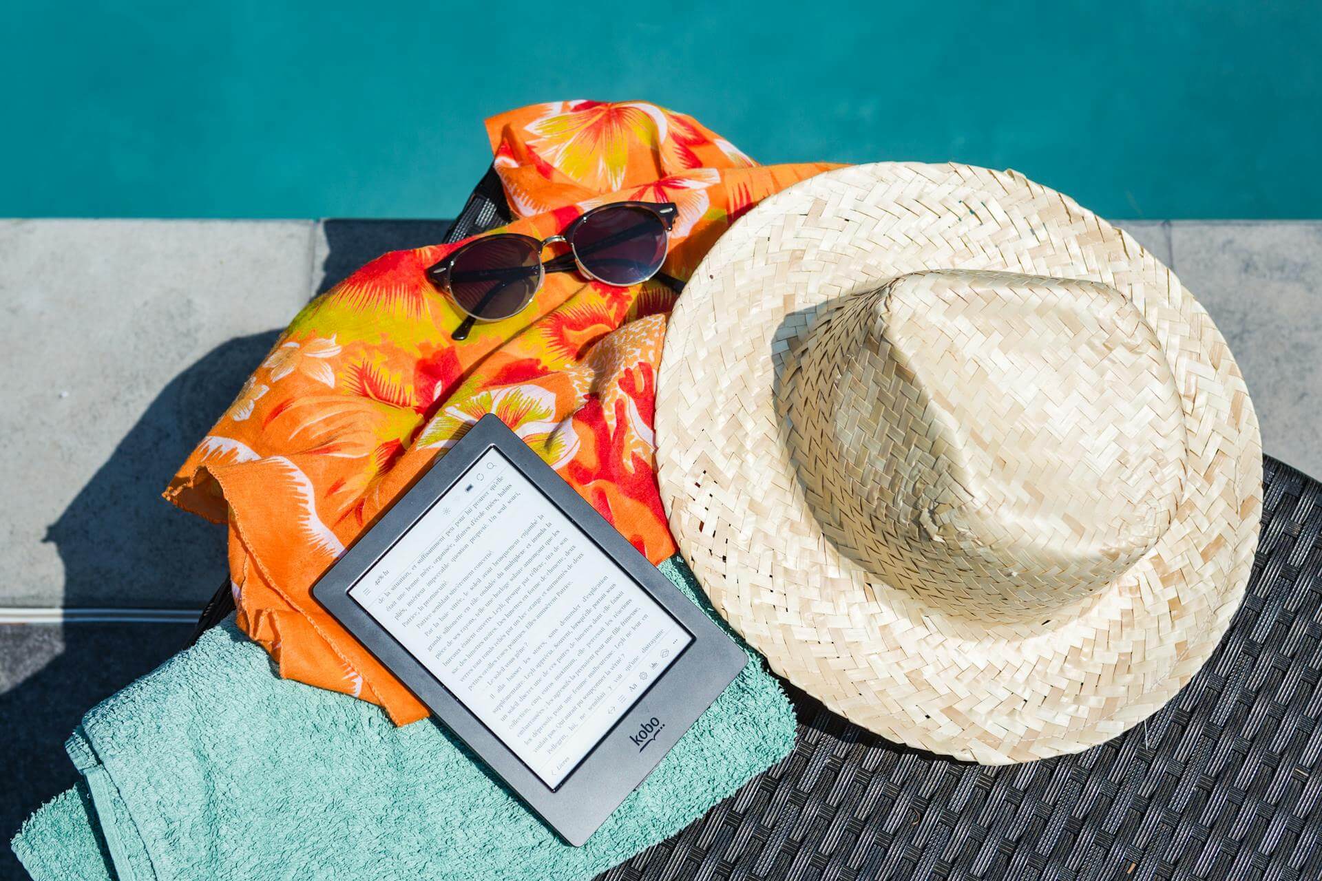 Towel, hat, sunglasses, and e-reader beside the pool